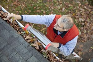 Man up ladder cleaning leafs out of gutter on house
