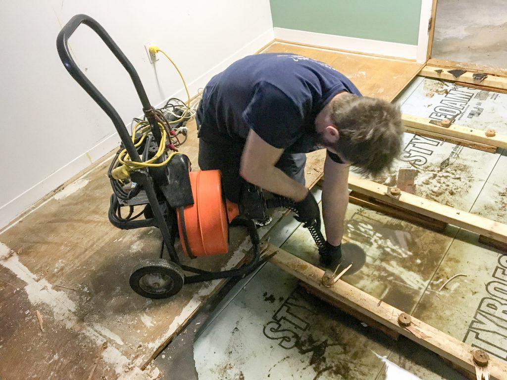 Plumber pushing a plunger drain into drain to unclog it