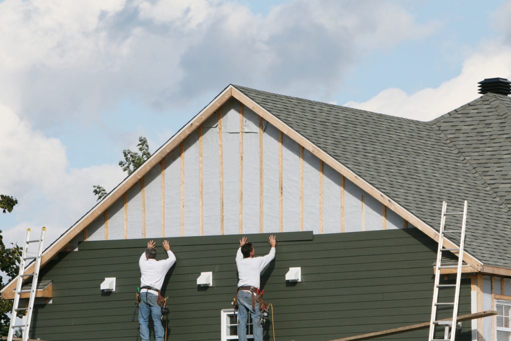 Two men applying green paneling to a house