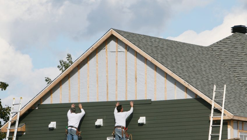 Two men applying green paneling to a house